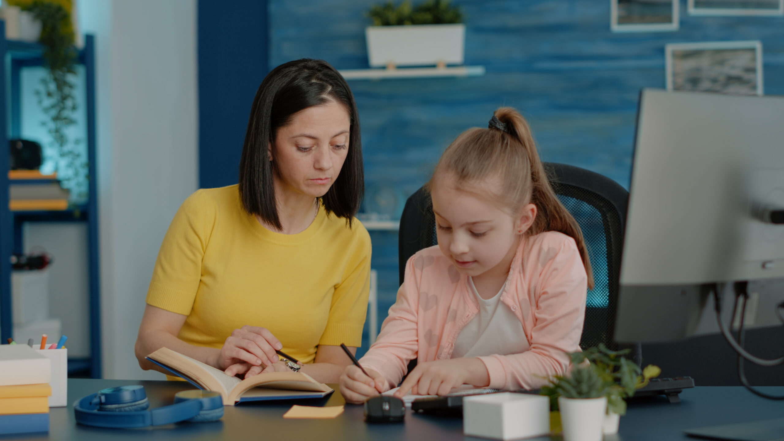 schoolgirl writing on notebook and checking book for information